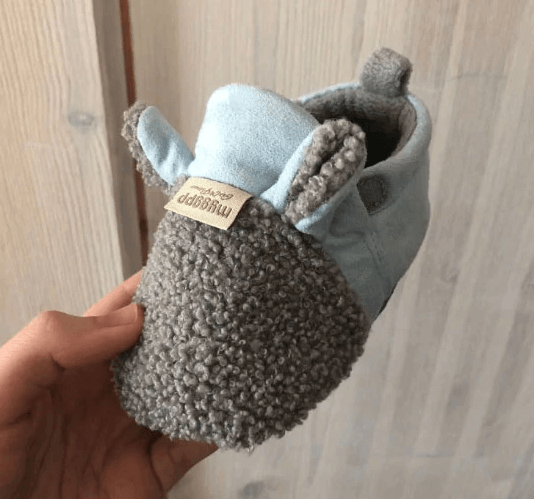 Helkroppsbilde av en baby med lamme-design, sko synlige, sittende, glad, myke første sko