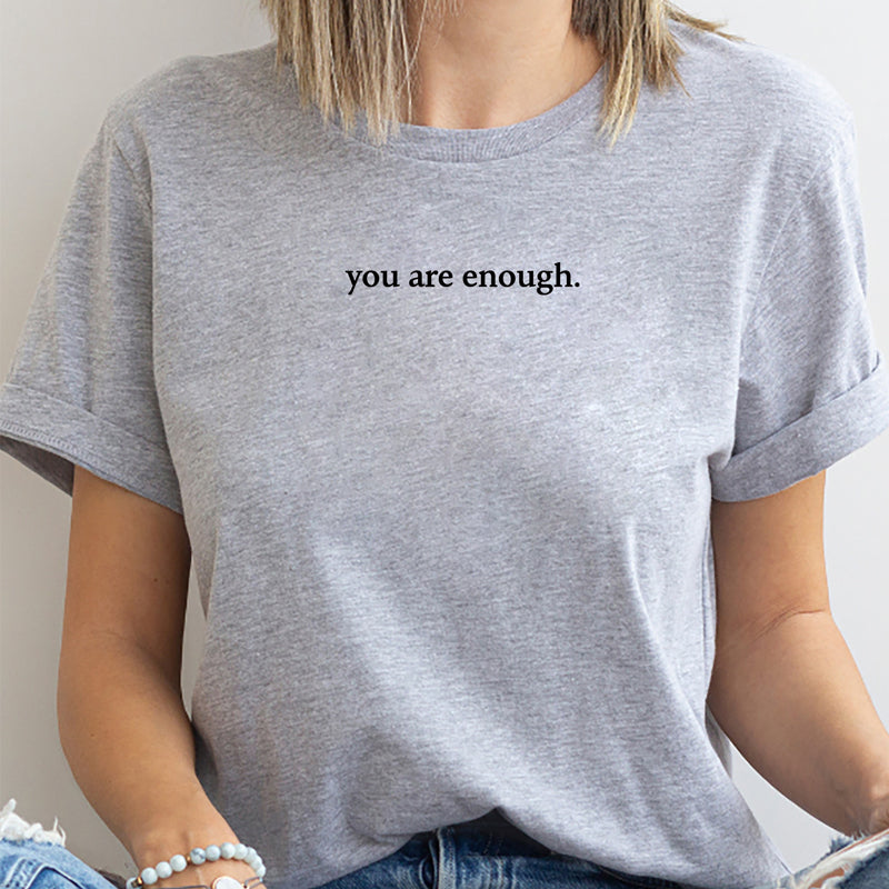 En kvinne smiler mens hun bærer sin inspirerende 'You are Enough' dame t-skjorte. Positivt plagg.