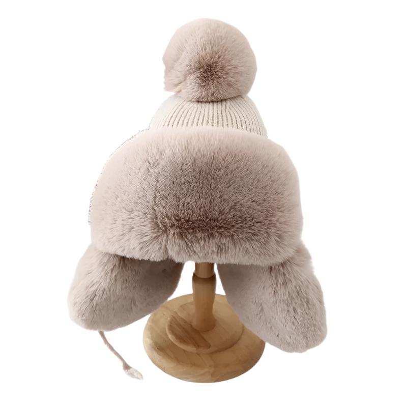 Myk strikket dame vinterlue med øreklaffer og fluffy dusk, sikrer varme og komfort.