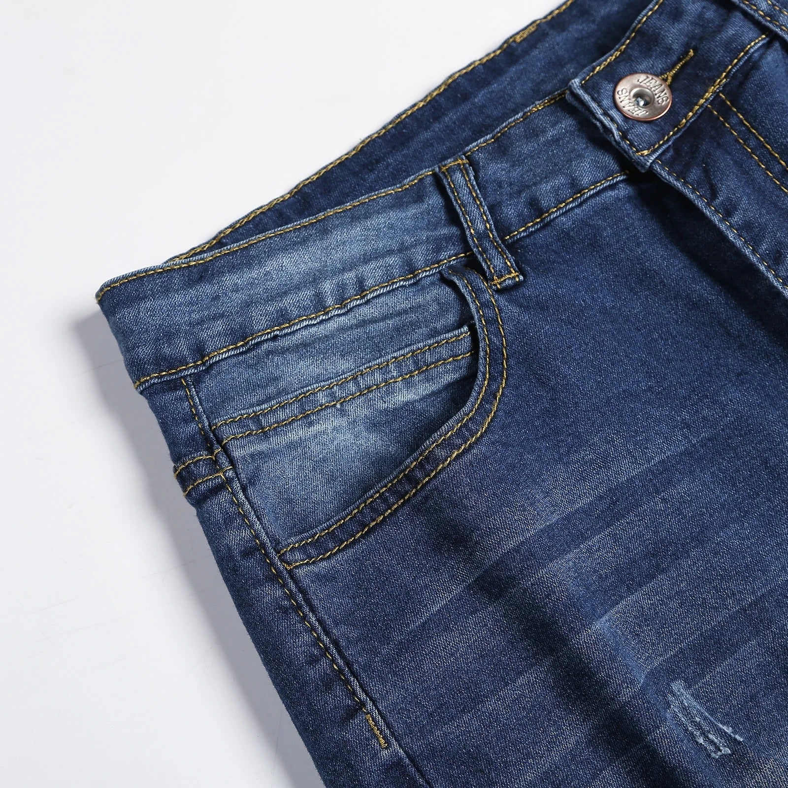 Detaljbilde av slitasje- og vaskeeffekter på jeans med smal passform for menn