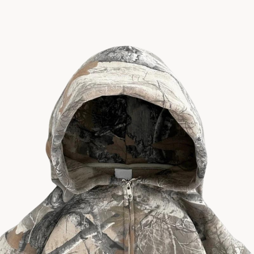 Mann iført en oversized grå kamuflasje hoodie, fremviser avslappet stil og komfort. Perfekt for hverdagsbruk.