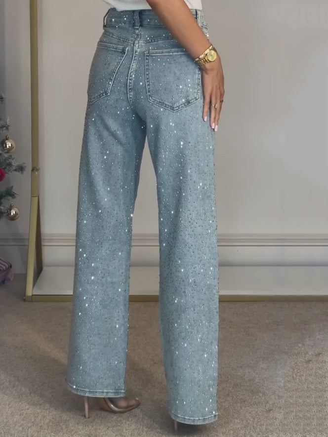 Nærbilde av glitrende detaljer på mørkeblå damejeans med høy midje, viser tekstur og stil.