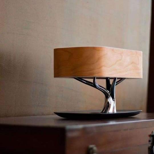 Minimalistisk tre skrivebordslampe med trådløs ladefunksjon for smarttelefon og innebygd Bluetooth høyttaler.