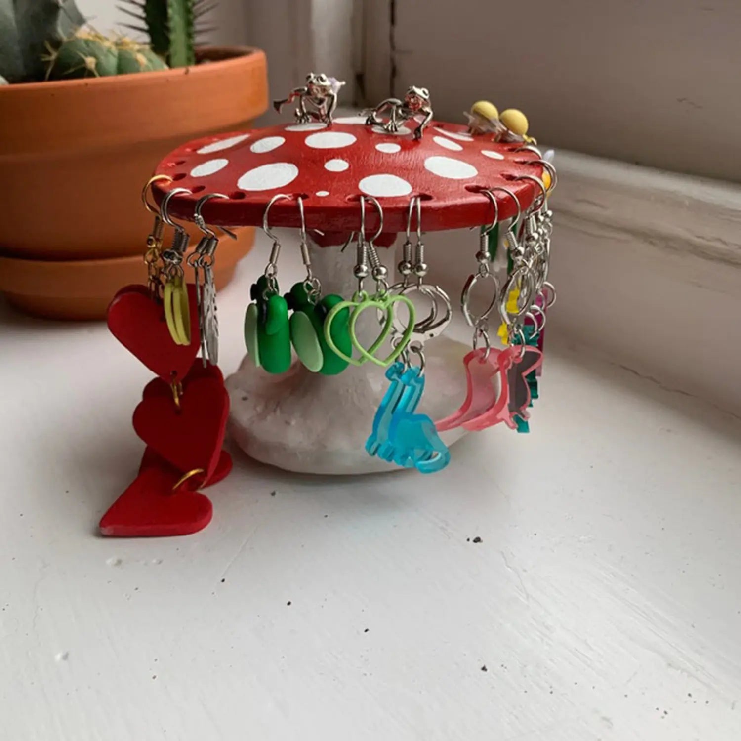 Sopp smykkeholder på et bord, rød og rosa farger gir et lekent preg. Organiserer smykker med sjarm.