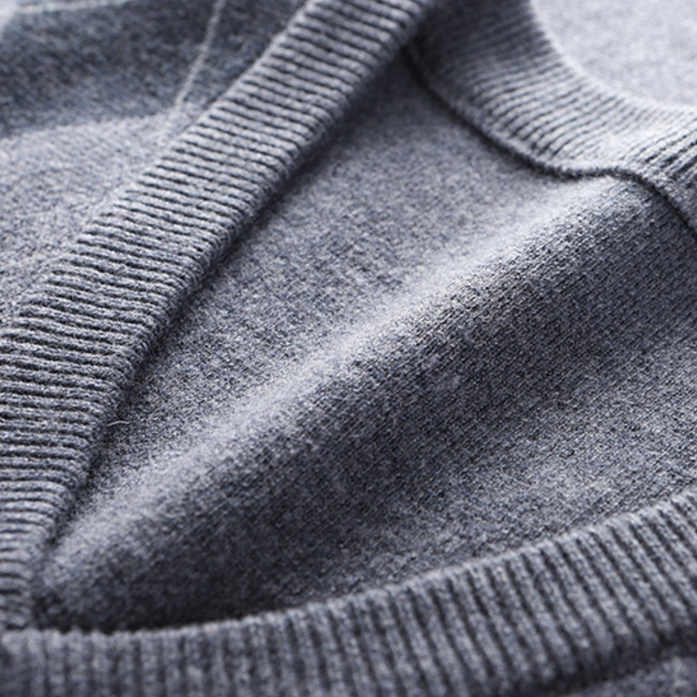 Nærbilde av V-halsen på en ermeløs herresweater. Viser strikkekvalitet og elegant snitt for lag-på-lag stil.