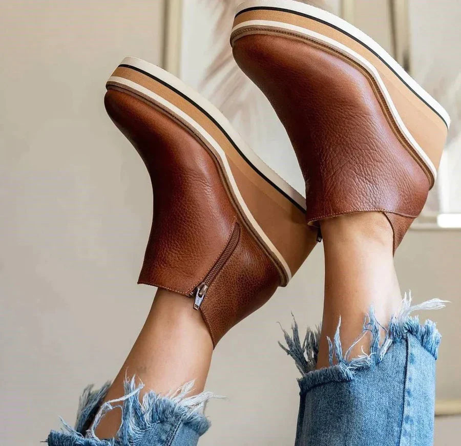 En kvinne sitter på sofaen, holder og masserer foten sin