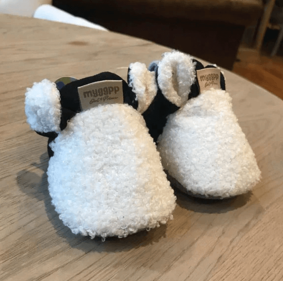 Babyschuhe im Lamm Design vor verschwommenem Hintergrund, weiche Baumwolle, rutschfest, kuschelige Erstlingsschuhe