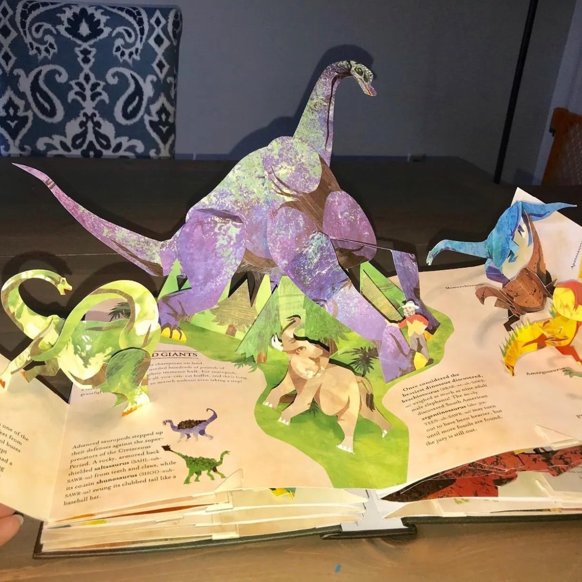 Åpen 3D dinosaurbok viser fargerike popup-scener, perfekt for barns læring og interaktiv lek.