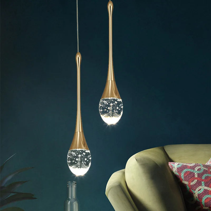 Nærbilde av gull dråpeformet pendellampe som avgir varmt lys. Moderne taklampe for stilfulle rom.