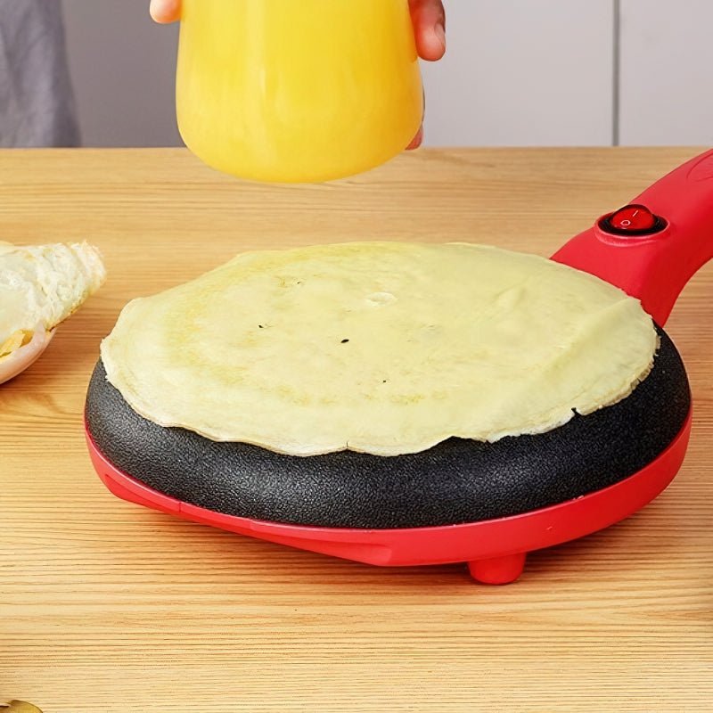 Nærbilde av en elektrisk crepepanne i bruk, lager en gyllen pannekake. Ideell for frokostmatlaging.