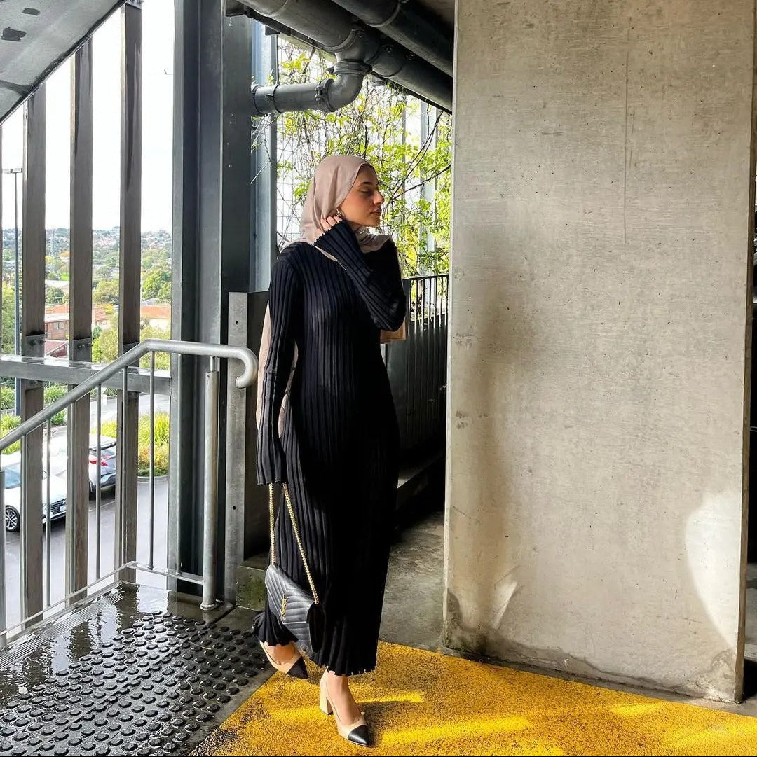 Kvinne sittende i en komfortabel, løs strikket kjole, viser allsidighet og elegant hverdagsluksus.