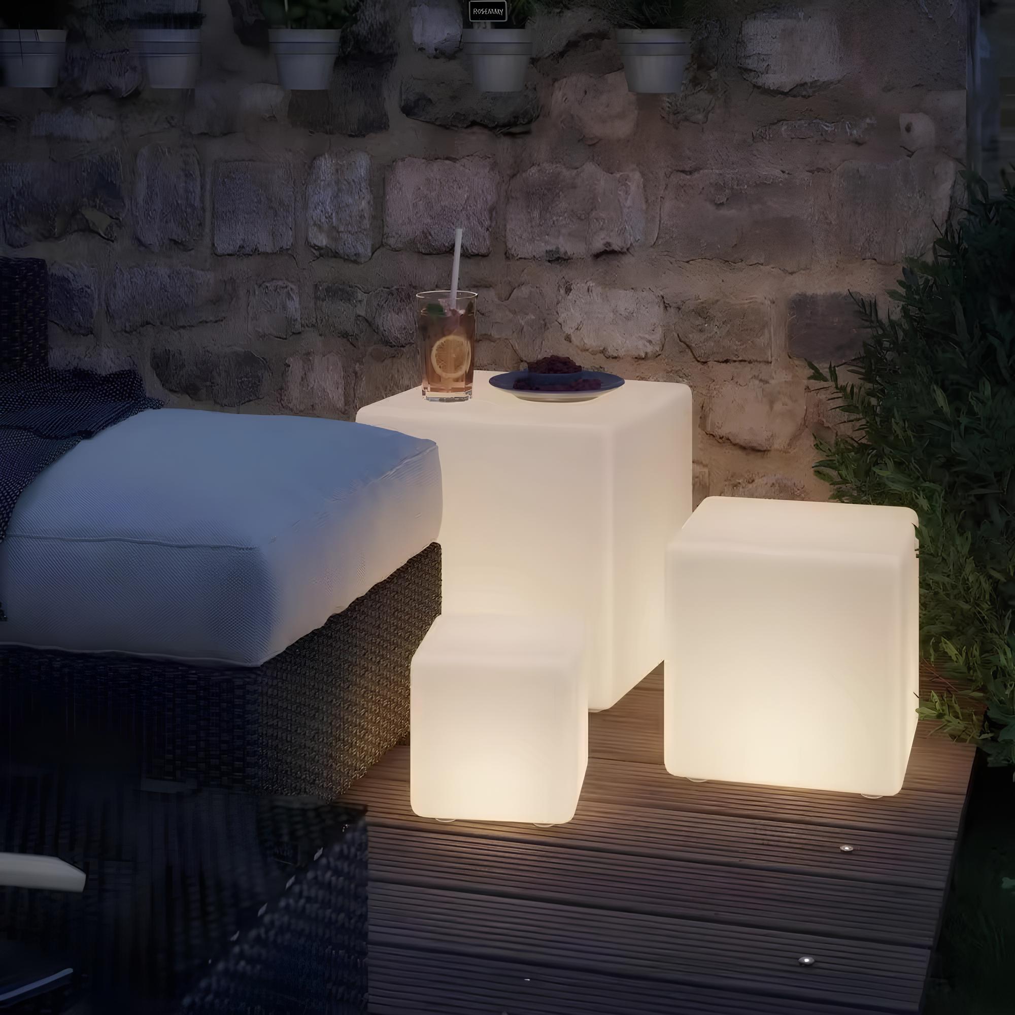 Flere kubeformede LED lamper lyser opp hagen med varierende flerfarget lys. Moderne utendørs belysning.