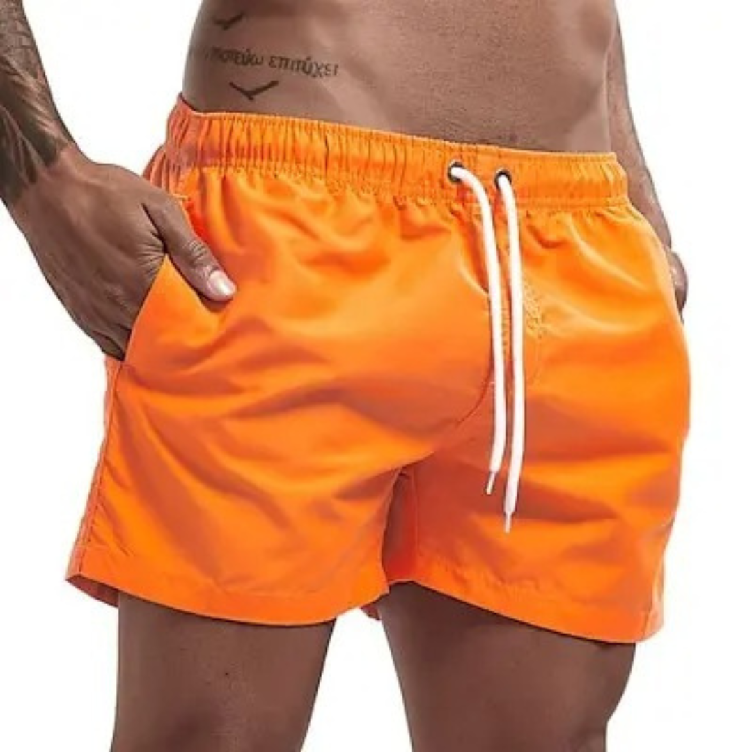 Ung mann poserer i gule, hurtigtørkende herre badeshorts ved bassenget.