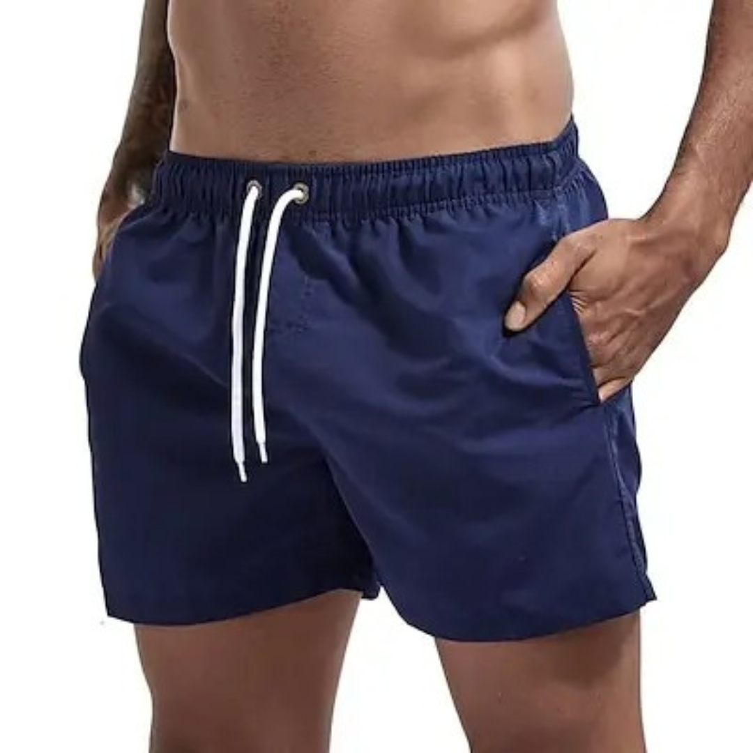 Grå, hurtigtørkende herre badeshorts som ligger på et håndkle ved bassengkanten.