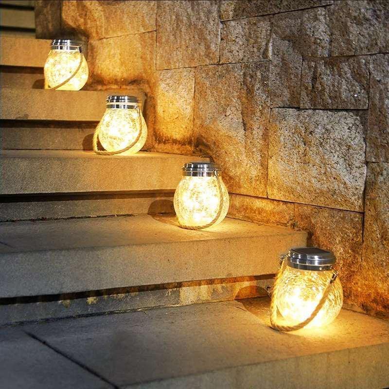 Solcellelampe i sprukket glass med hampsnor henger i en hage, klar til å gi stemningslys om kvelden.